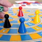 Hand rolling a green dice over a colorful board game with black, red, yellow, and blue pawns, representing gamification in speech therapy.