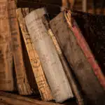 A close-up view of several old, worn books with weathered covers and pages, leaning on a shelf.