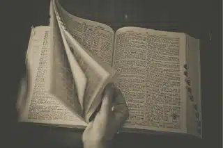 Sepia photograph of a person flipping through the pages of a large dictionary, symbolizing traditional vocabulary lookup.