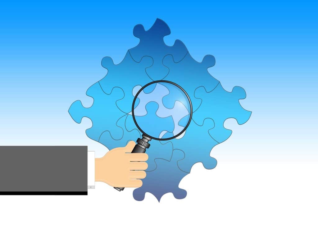 A hand holding a magnifying glass over a blue puzzle, with one piece highlighted, illustrating the concept of breaking down complex tasks and focusing on smaller parts for learning.