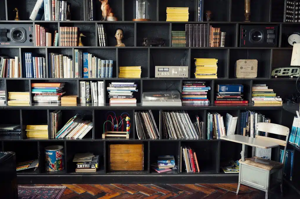 A tall, dark wooden bookshelf unit filled with rows of diverse and colorful books, along with some decorative items and media.