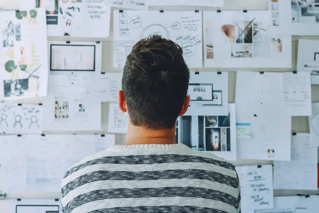 The back of a person looking at a bulletin board densely covered with papers and notes, symbolizing the overwhelming feeling of managing numerous IEP meetings and speech therapy goals.