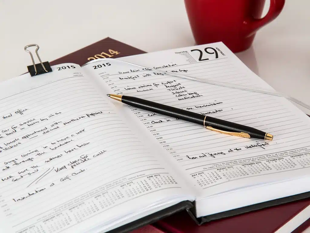 An open daily planner with handwritten notes and a black pen, next to a red coffee mug, symbolizing organization and control over one's schedule.