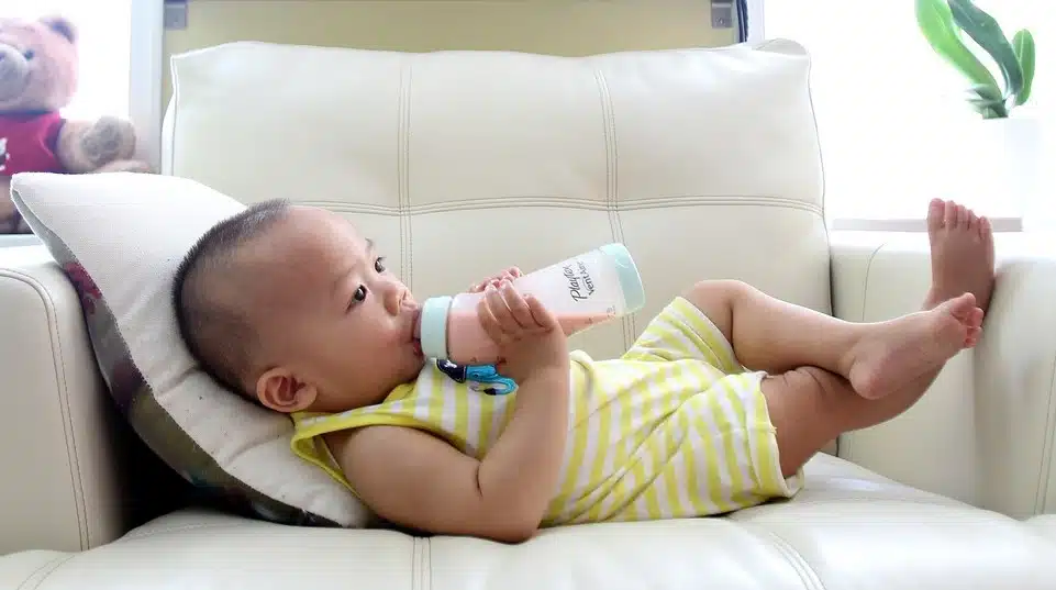 Photo of a baby relaxed on a couch, self-feeding from a bottle, illustrating potential challenges with sucking and latching.