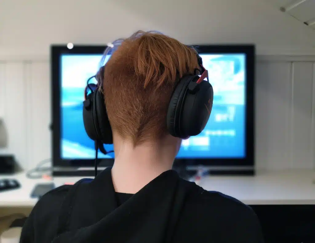 Teen boy wearing headphones intently focused on a monitor, symbolizing digital game engagement and online gamification in speech therapy.