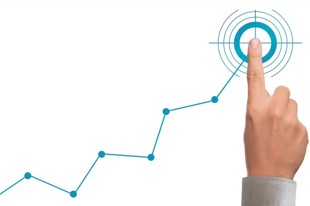 Illustration of an upward-trending data line graph, leading to a target at the top, with a human hand's index finger placed on the target, symbolizing consistent progress towards a measurable goal.