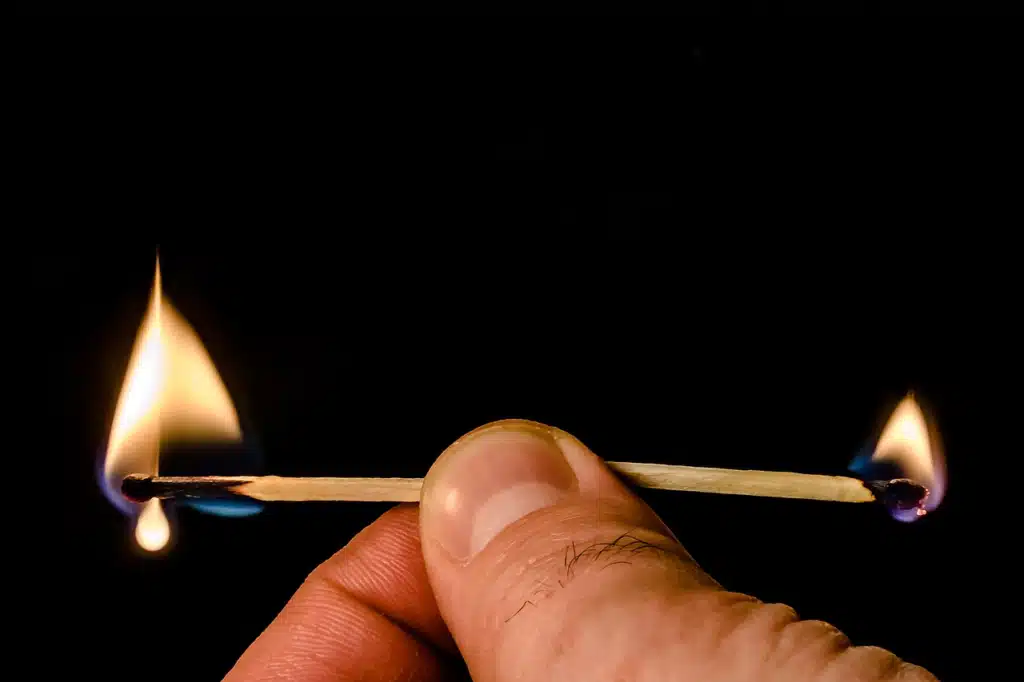 A close-up of a hand holding a matchstick lit and burning brightly at both ends, symbolizing intense pressure, exhaustion, and teacher burnout.