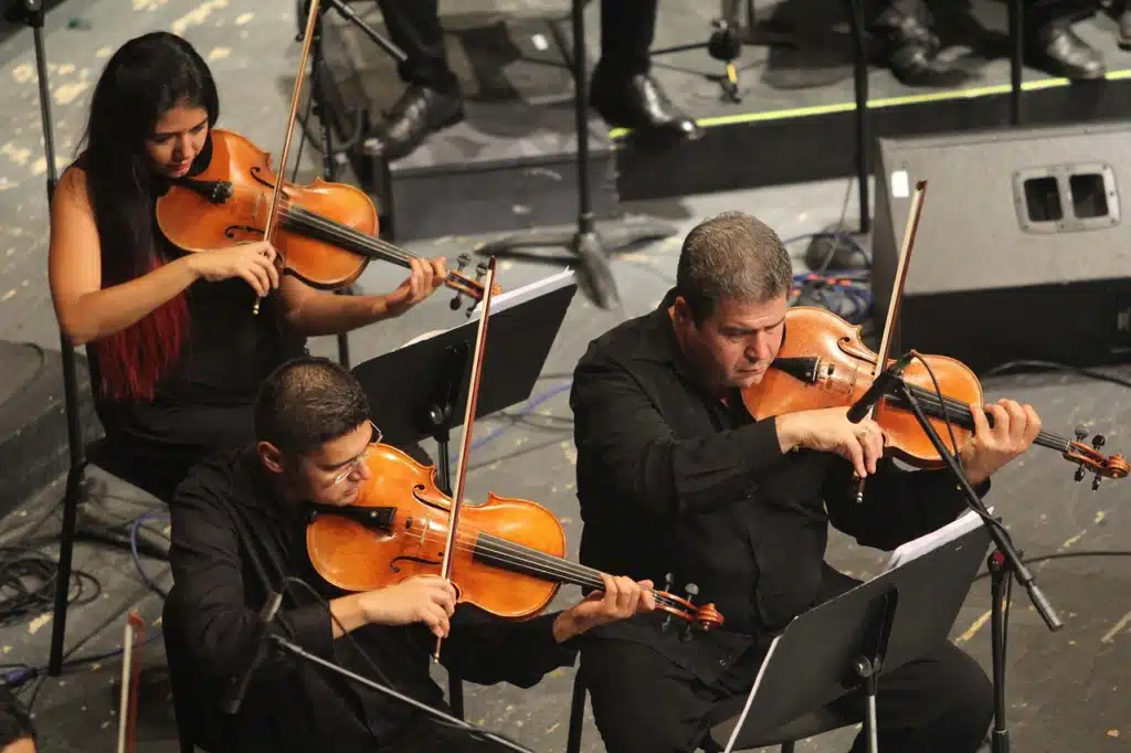 Three orchestra musicians deeply focused on playing their string instruments, symbolizing the concentrated effort and practice needed for deep learning in language therapy.