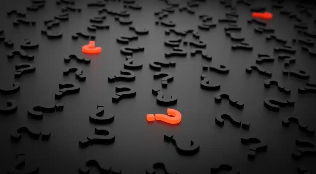A dark surface covered with numerous black question mark symbols lying flat, with three prominent, glowing orange question mark symbols standing upright.