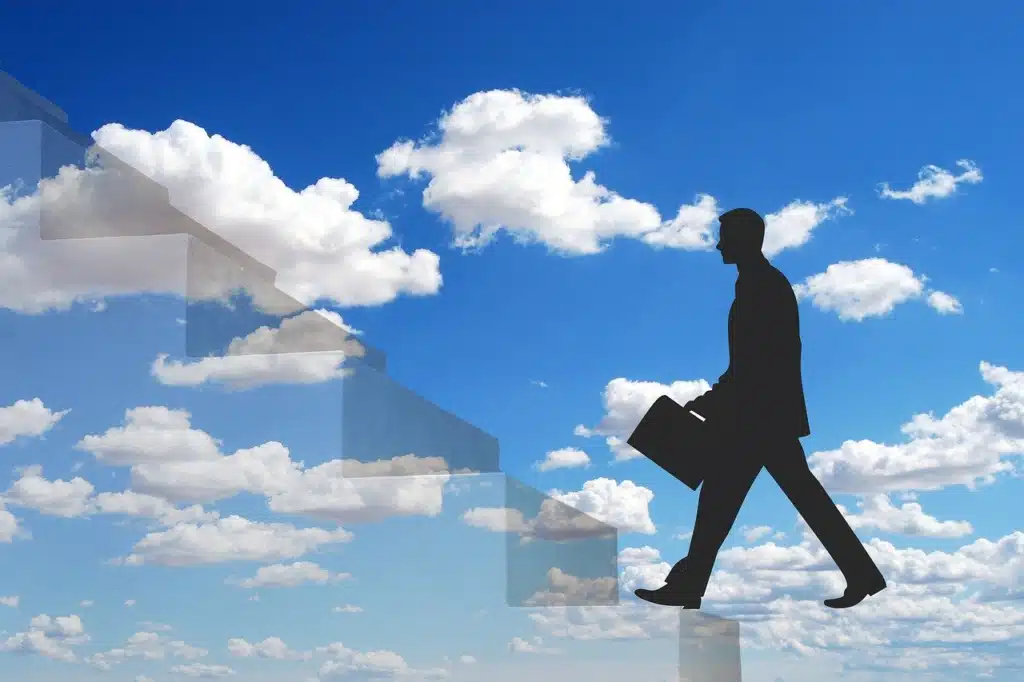 A dark silhouette of a person in a suit carrying a briefcase walking on a path made of transparent stairs against a bright blue sky with clouds, symbolizing the limited, upward-only career advancement path in education that often leads away from the classroom.