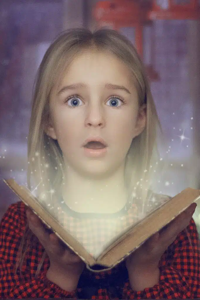 A young girl with light hair and wide, surprised blue eyes, holding an old, open book from which light and magical sparkles emanate.