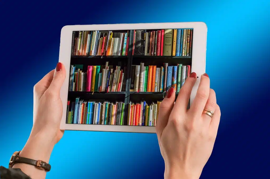 Two hands holding a white tablet, which displays a digital bookshelf filled with colorful book spines against a blue background.