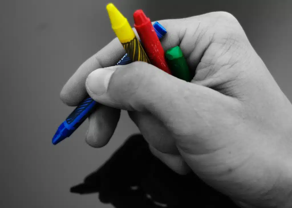 Black and white photo of a hand holding a variety of colorful crayons. Represents differentiated instruction for diverse learning styles.
