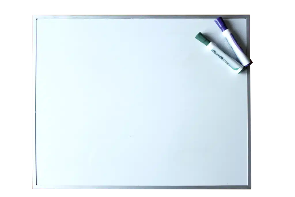 A blank white dry-erase board with a silver frame, with two dry-erase markers (one green, one purple) resting in the top right corner.