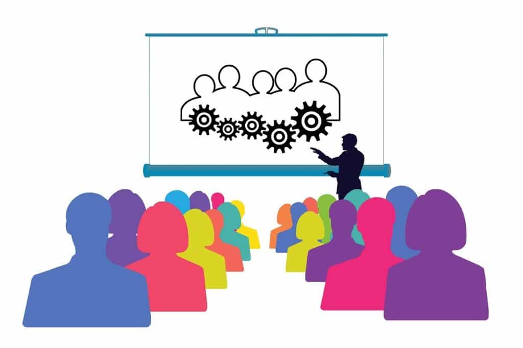 A silhouette of a speaker giving a presentation to a diverse, multi-colored audience. The screen displays a diagram of interconnected human figures and gears, symbolizing collaborative professional development assisted by AI.