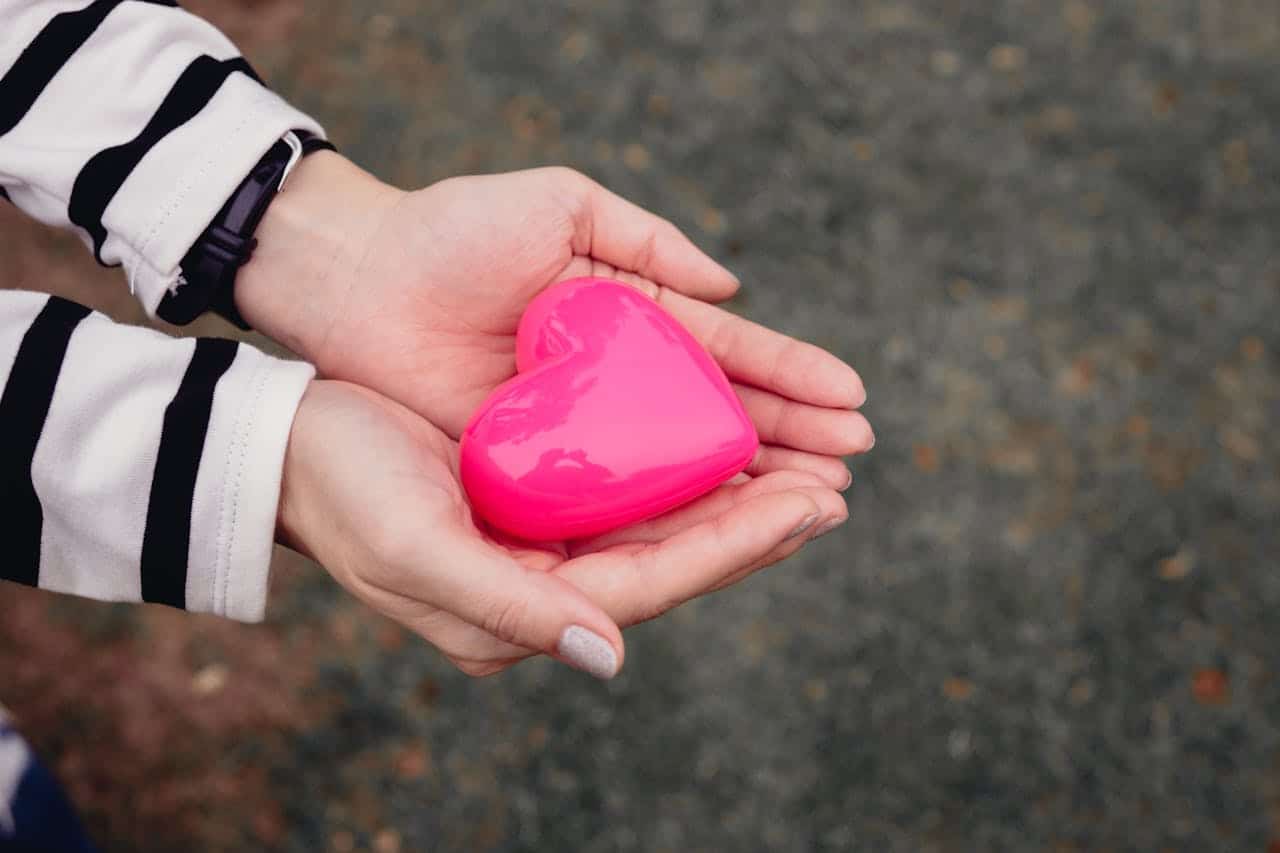 cta-01 Close-up of hands holding a pink heart-shaped toy outdoors, symbolizing love and care.
