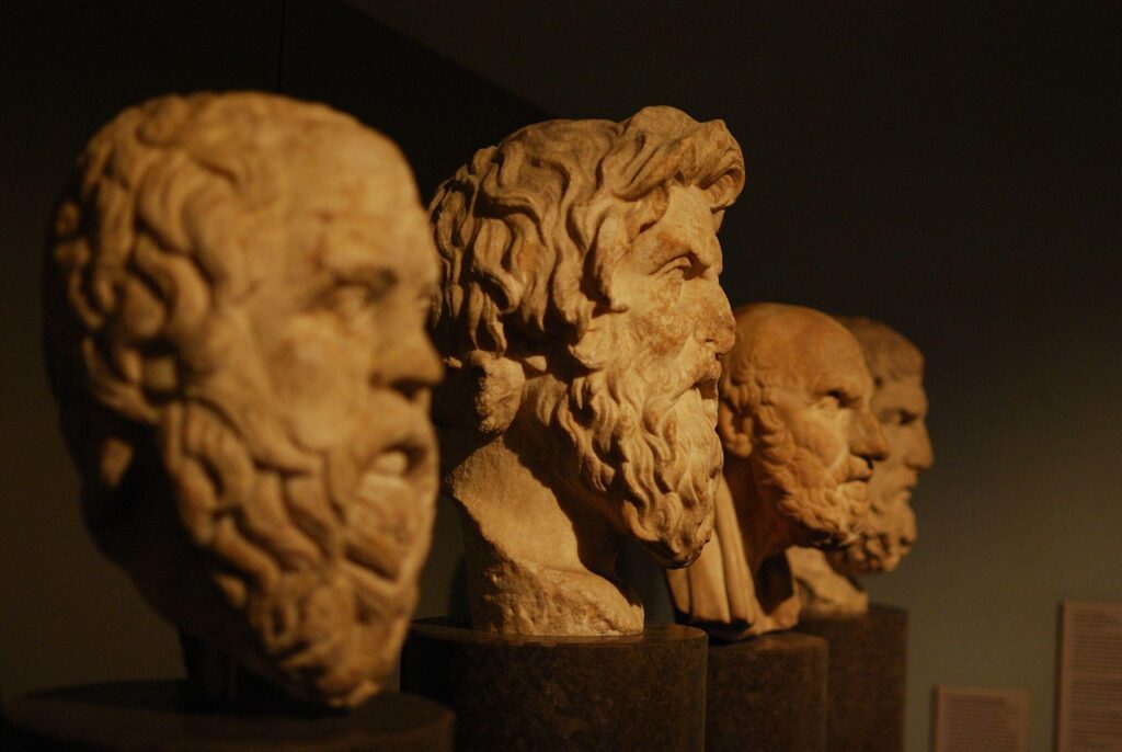 A row of stone busts of bearded ancient Greek philosophers (Socrates, Plato, etc.), dimly lit in a museum setting.